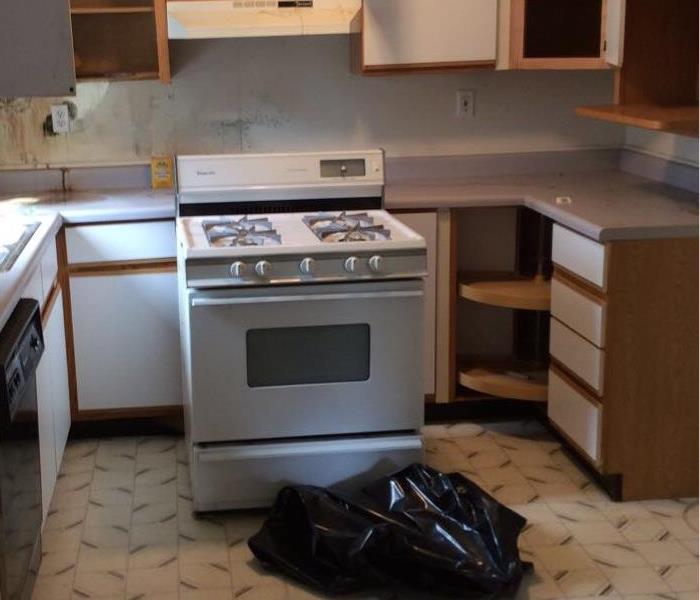 A kitchen with a trash bag and a stove moved away from cabinets. The cabinets are open.