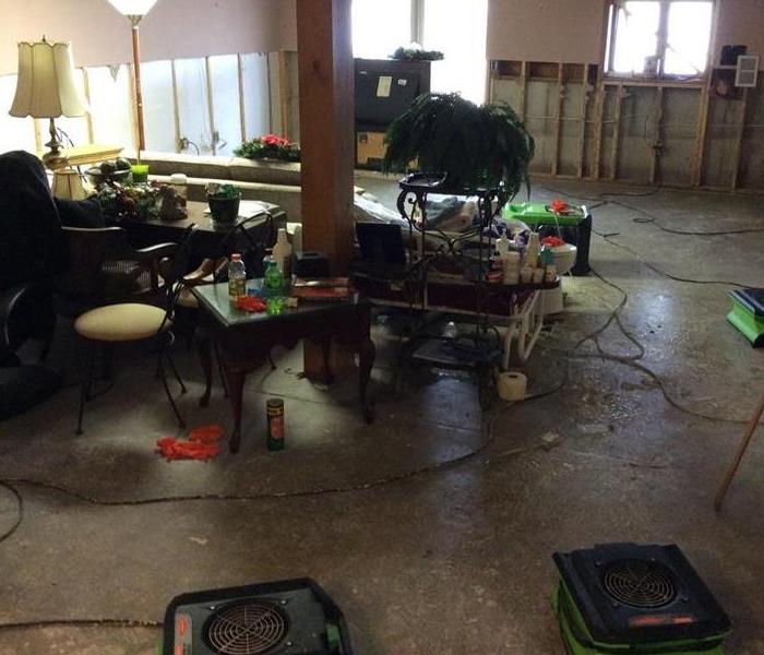 A basement with ripped out flooring and drywall along with SERVPRO equipment and homeowners belongings