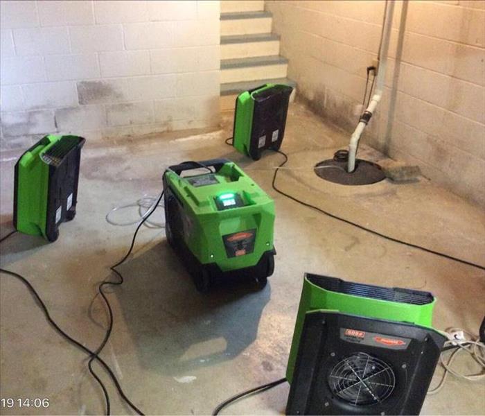 A photo of a dehumidifier and 3 fans surrounding it in a white unfinished basement